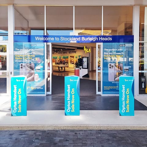 Shop Display with Door and Window Signage for Yes Optus Burleigh, print and install by Ziggiz Print & Signs, Loganholme with Custom Corflute Bollards from elongated Stackable Advertising Cubes